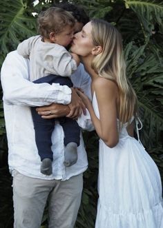 a woman kissing a little boy in front of some trees