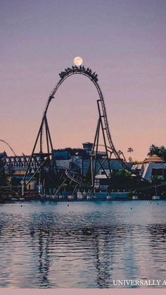 an amusement park with a full moon in the sky above it and water reflecting on the ground