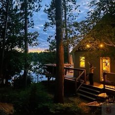 a person standing on the porch of a cabin at night with trees and water in the background