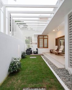 an outdoor living area with grass and rocks in the foreground, covered by a white pergolated roof