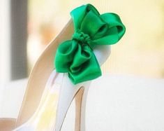 a shoe with a green bow on the side and white shoes in the back ground