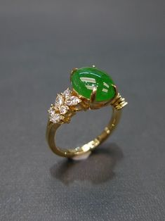 a gold ring with an oval green stone surrounded by three small white stones on the side