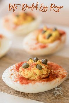 deviled eggs are topped with red sauce and pistachio seeds on a wooden board