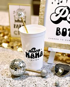 a white cup sitting on top of a table next to sunglasses and a disco ball