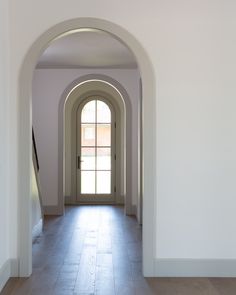 an archway leading into a white room with wooden flooring and tile on the ground