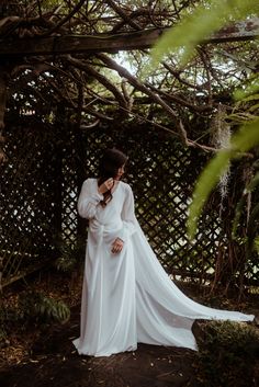 a woman in a white dress standing under a tree with her arms around her neck