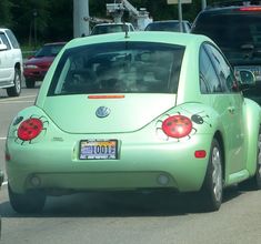 a green car with ladybugs painted on the rear window is driving down the street