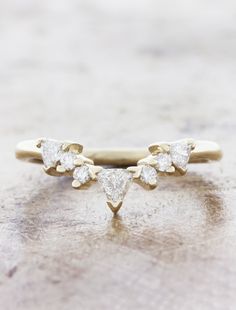 a gold ring with three pear shaped diamonds on it, sitting on top of a rock