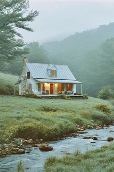 a small white house sitting on top of a lush green hillside next to a river