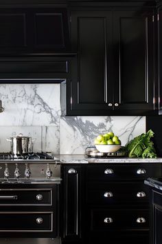 a kitchen with black cabinets, marble counter tops and stainless steel stove top ovens