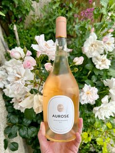 a person holding up a bottle of wine in front of some white and pink flowers