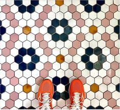 a pair of orange shoes standing on top of a white and blue tiled floor with hexagonal tiles