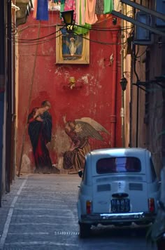 an old car parked on the side of a street next to a wall with paintings