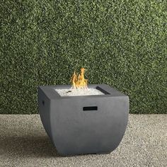 a concrete fire pit sitting on top of a gravel ground next to a green wall