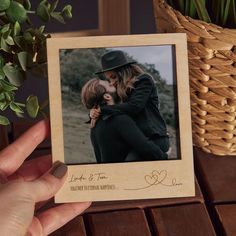 a hand holding a wooden photo frame with a couple kissing