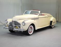 an old fashioned car is parked in a large room with curtains on the wall behind it