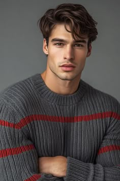 a young man with his arms crossed wearing a gray and red striped sweater, looking at the camera