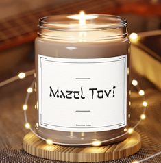 a candle that is sitting on a table with some string lights around it and the words hazel tov written in black