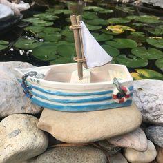 a small sailboat sitting on top of rocks next to water and lilypads