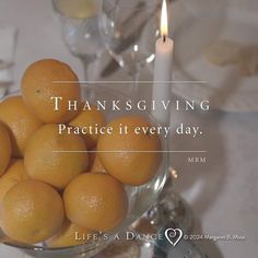 a glass bowl filled with oranges sitting on top of a table next to a candle