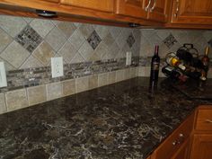 a granite counter top in a kitchen with wooden cabinets and wine bottles on the shelf