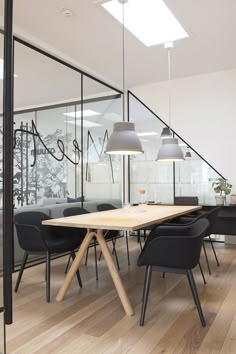 a wooden table sitting in front of a glass wall with black chairs and lamps on it