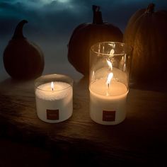 two candles sitting next to each other on a wooden table in front of pumpkins