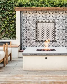 an outdoor fire pit in the middle of a patio with chairs around it and a tiled wall behind it