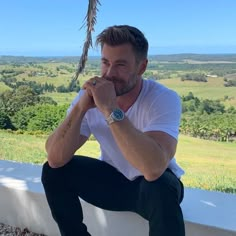 a man sitting on top of a cement wall next to a palm tree and looking at the camera