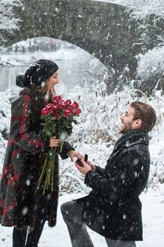 a man kneeling down next to a woman holding flowers in the snow while she holds out her hand