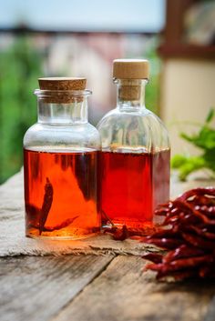 two bottles filled with liquid sitting on top of a wooden table next to chili peppers