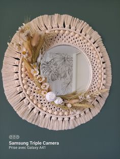 a round mirror hanging on the wall next to a plant and some feathers in front of it