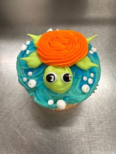 a cupcake decorated with an orange flower and blue icing on a silver surface