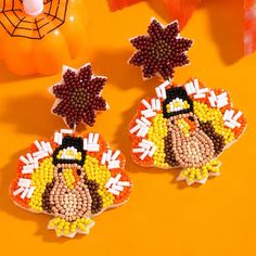 two pairs of beaded thanksgiving turkey earrings on an orange table with pumpkins and decorations