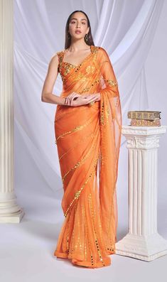 Introducing our vibrant orange organza sari, meticulously crafted from a luxurious blend of organza and tulle. The pallu features intricate gold metallic and acrylic embroidery, forming delicate lines that add elegance. The pre-stitched tulle bottom provides a graceful finish. Complementing the sari is a matching tulle blouse, adorned with abstract gold and chunky embroidery, blending metallic shapes and acrylics for a chic, stylish look. Elegant Organza Pre-draped Saree For Navratri, Gold Organza Pre-draped Saree For Navratri, Gold Organza Pre-draped Saree With Resham Embroidery, Organza Blouse Piece For Reception And Diwali, Organza Blouse Piece For Diwali Reception, Pre-draped Organza Saree With Gota Work, Organza Pre-draped Saree For Reception Diwali, Anarkali Pre-draped Saree With Gota Work, Festive Organza Pre-draped Saree With Pallu