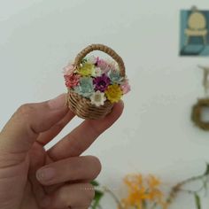 a hand holding a miniature basket with flowers in it and a wall decoration behind it