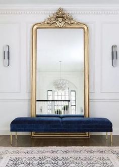 a blue bench sitting in front of a large gold framed mirror on a white wall