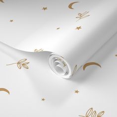 a white wallpaper with gold stars and crescents on it's side, next to a paper roll