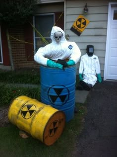 two people in white suits are standing next to barrels with radioactive symbols on them and one is wearing a radiation suit