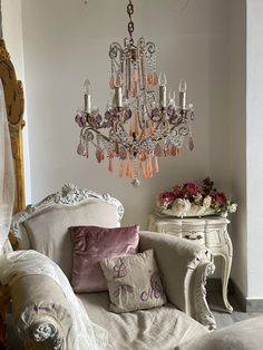 a chandelier hanging from the ceiling in a room with white furniture and flowers