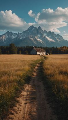 a dirt road leading to a house with mountains in the background