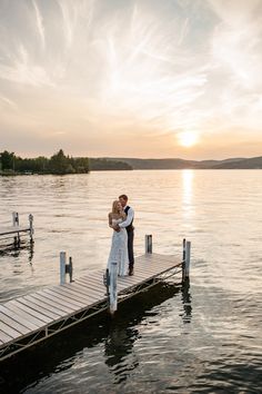 a bride and groom standing on a dock at sunset