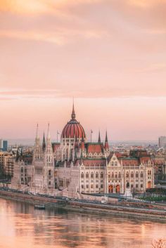 the hungarian parliament building in budapest is seen from across the river at sunset with pink clouds