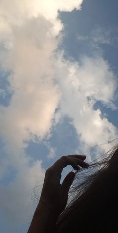 a woman is holding her hand up to the sky with clouds in the back ground