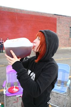 a woman with red hair is drinking from a plastic container in front of some chairs