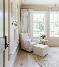 a white chair and ottoman in a room with large windows, rugs and curtains