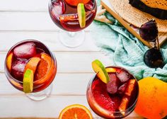 three glasses filled with different types of drinks on top of a wooden table next to an orange slice