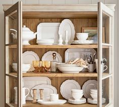 a cabinet filled with white dishes and plates on top of wooden shelves next to a wall