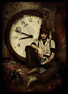 a man sitting in front of a large clock with his hands on his hipster pants