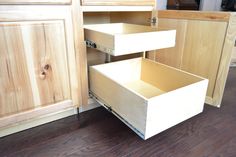 an open drawer in the middle of a kitchen with wood floors and cabinets behind it